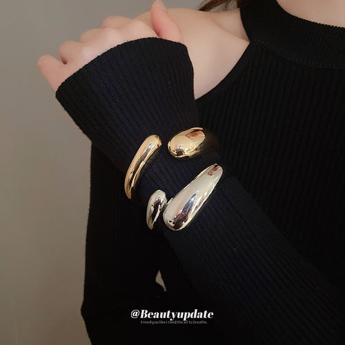 three gold-tone or silver-tone open hinged bracelets with smooth teardrop ends shown worn in a styled second view