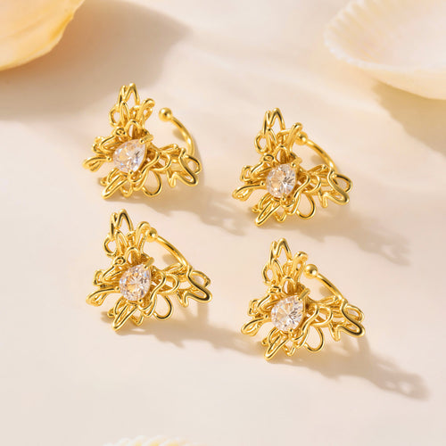 Four gold butterfly ear cuffs with teardrop stones on beige with shells