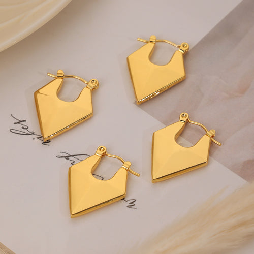 Four gold faceted diamond shape hoop earrings on paper surface
