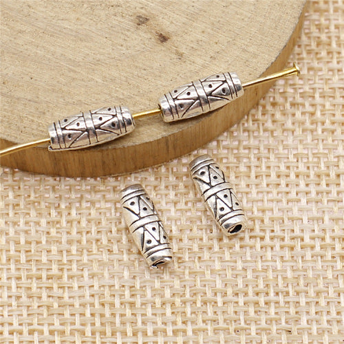 Single piece on a rustic surface of engraved geometric tube small-hole bead in two antique finishes