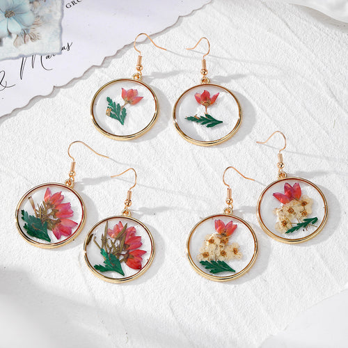 Three pairs of gold round resin pressed flower earrings on white fabric