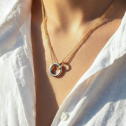 Close-up of two-tone gold and silver interlocking circle pendant on white shirt