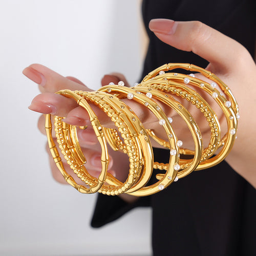 Hands holding stacked gold bamboo bead pearl and zircon cuff bracelets