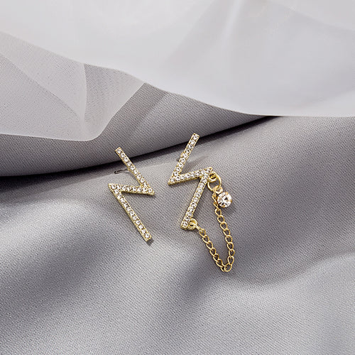 Gold pavé lightning asymmetric studs with chain on gray fabric
