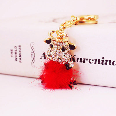 Angled front view of the rhinestone cow charm above a bright red fluffy pom pom.