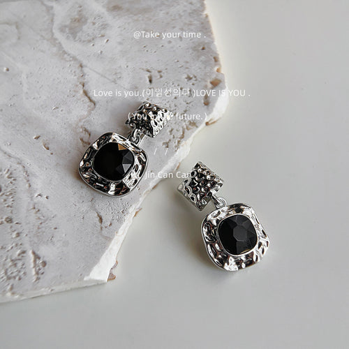 Silver hammered square drops with black stones on white stone prop
