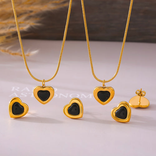 Two gold black-heart necklaces and studs laid on book page