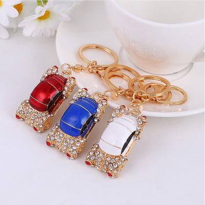 Three vintage car keychains in red, blue, and white with gold rings by teacup