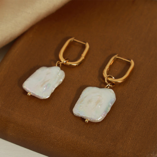 Pair of gold huggie irregular pearl drops on brown wood board