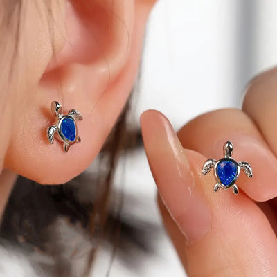 Silver blue opal turtle stud worn on ear with matching stud held by fingers