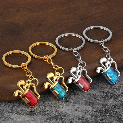 Four golf bag and club keychains shown in gold-tone and silver-tone finishes with red and blue panels.