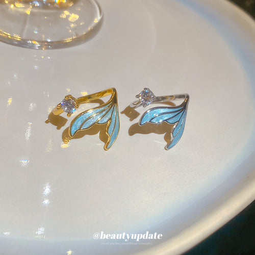 Gold and silver blue mermaid tail rings side by side on white plate