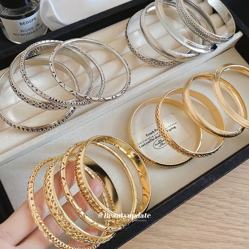 Assorted gold and silver textured bangles arranged in black jewelry tray