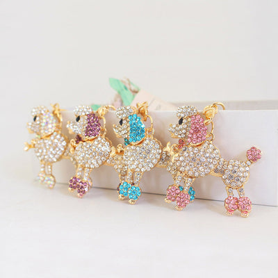 Four rhinestone poodle keychains with white, purple, blue and pink accents stand in a row.