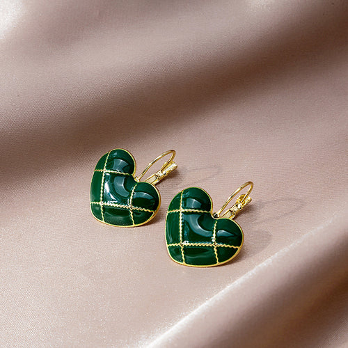 Close-up of green enamel heart earrings with gold grid on pink fabric