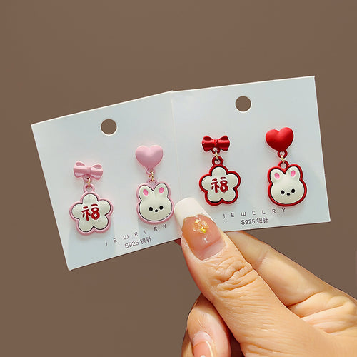 Red and pink bunny Fu flower enamel stud pairs on jewelry cards in hand