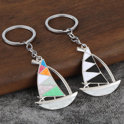 Two silver-tone sailboat keychains with multicolor and black sail panels on a wood and gray surface.