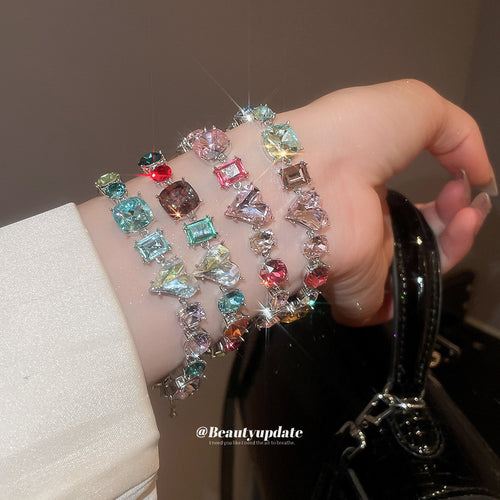 Three multicolor crystal heart bracelets stacked on wrist near black bag