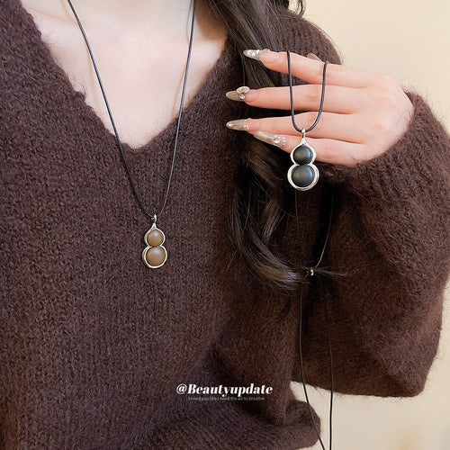 A stacked double-gourd pendant in black and warm brown on a long black cord shown in a styled close-up