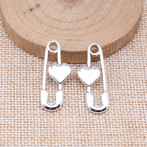 Heart-accent safety pin charms arranged on a natural wood surface