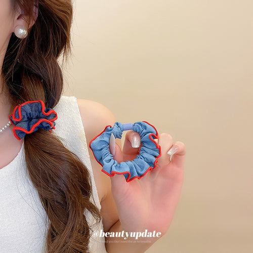 Light blue denim scrunchie held beside dark denim scrunchie worn in ponytail