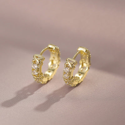 Gold X-cross clear stone huggie hoop earrings pair on pink fabric