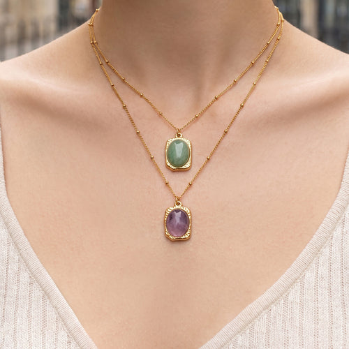 Model wearing layered gold green and purple oval stone pendant necklaces outdoors
