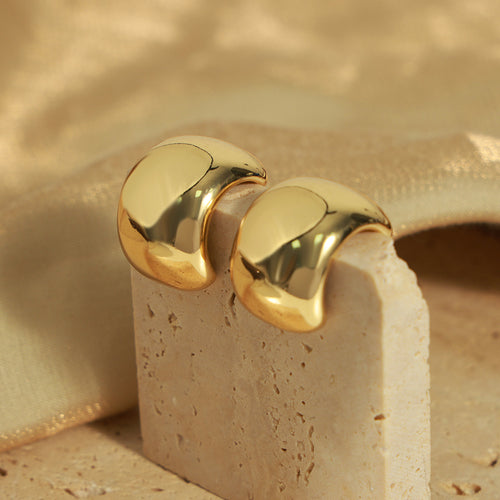 Pair of gold polished C-hoops resting on stone block
