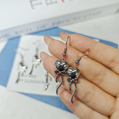 Hand holding silver bow heart drop earrings with ribbon tails