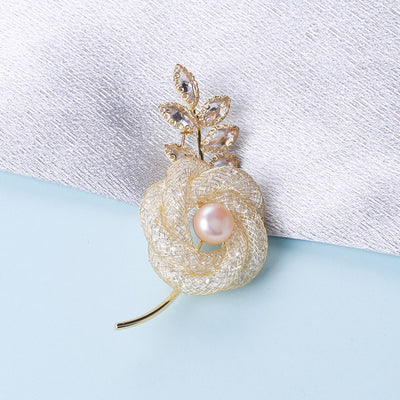 Gold mesh rose brooch pearl center on fabric background