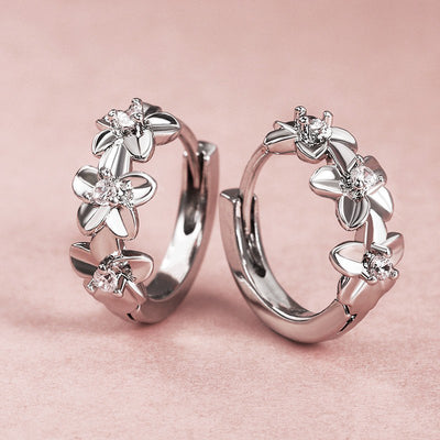 Silver flower huggie hoop earrings pair on pink textured surface