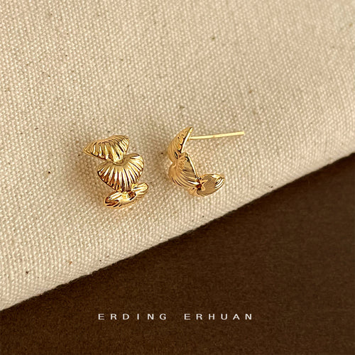 Pair of gold textured stacked heart studs on brown book edge