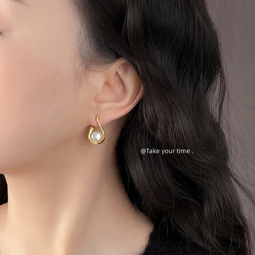Gold-tone open-teardrop-frame white-pearl studs shown worn on an ear.
