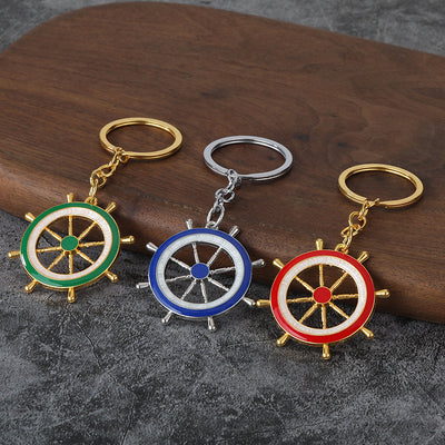 Three ship wheel keychains in green, blue, and red on a wood and gray surface.