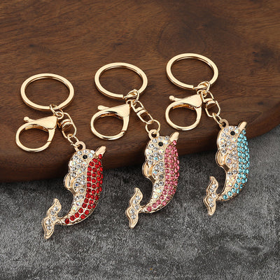 Three gold-tone dolphin keychains with red, pink, and sky blue rhinestones on a wooden surface.