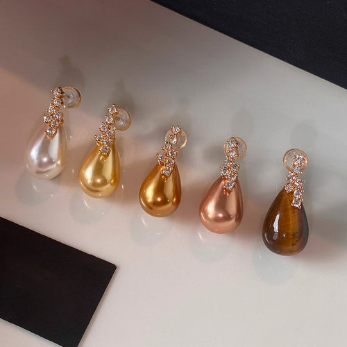 Styled wear view of 金色水滴珍珠耳钉 showing glossy gold-tone teardrop pearls beneath small clusters of clear stones