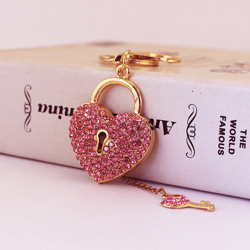 A pink rhinestone heart lock hangs beside a small pink key charm on a chain.