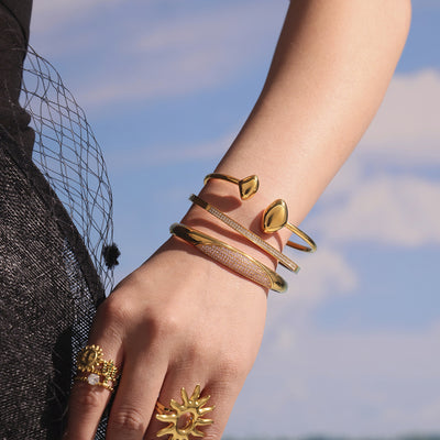 Wrist stacked gold hinged pavé bangle with other gold cuffs outdoor