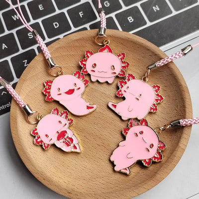 Five pink axolotl enamel phone charms with pink straps on wooden dish