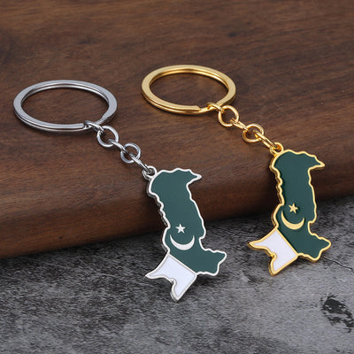 Silver-tone and gold-tone Pakistan map keychains displayed together on wood.