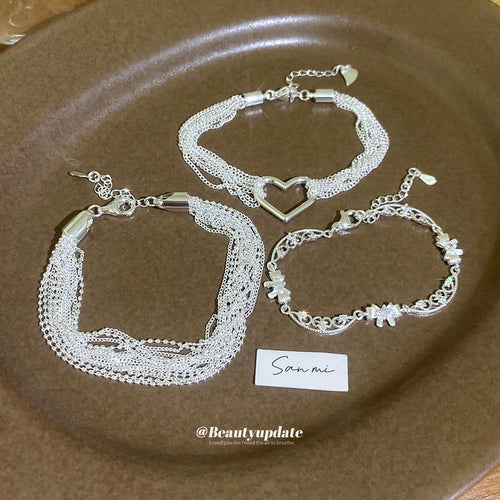 Three silver bracelet styles laid on brown plate with card