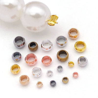 Metallic crimp bead jewelry findings arranged on a light background