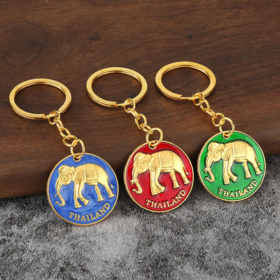 Three elephant medallion keychains in blue, red, and green rest on a wooden surface.