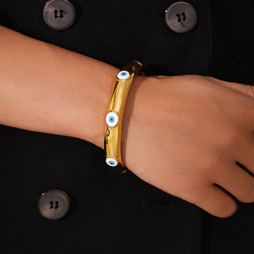 Wrist wearing gold evil-eye cuff over black coat sleeve