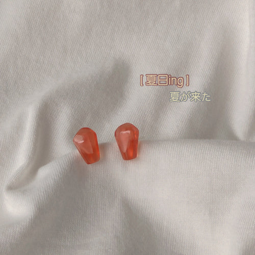 Pair of coral red resin seed studs on white fabric fold