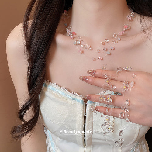 Model wearing pink chip bead necklace and holding clear flower strand necklace