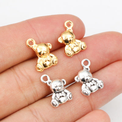 Overview of tiny seated teddy bear charms with sculpted faces in bright gold and silver-tone finishes arranged on a ligh