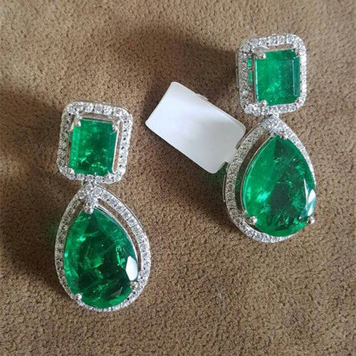 Green emerald and pear halo drop earrings on brown fabric