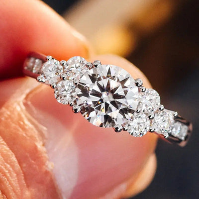 Silver round CZ cluster ring held between fingers close-up front