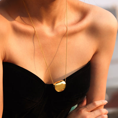 Model wearing long gold hollow bean oval pendant on black strap dress